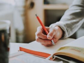 person holding on red pen while writing on book