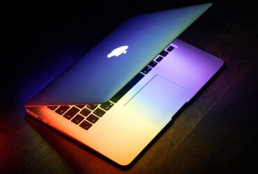 A MacBook lit up in rainbow colors on a wooden surface