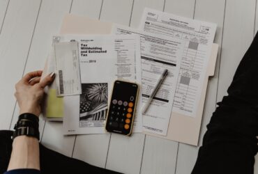 person holding paper near pen and calculator