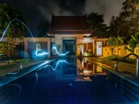 reflection of blue light crossing above pool near house during nighttime