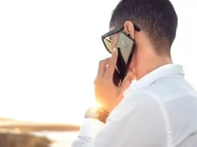 man holding smartphone standing in front of calm body of water