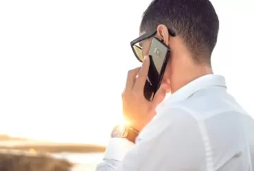 man holding smartphone standing in front of calm body of water