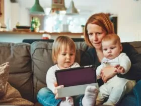 two babies and woman sitting on sofa while holding baby and watching on tablet